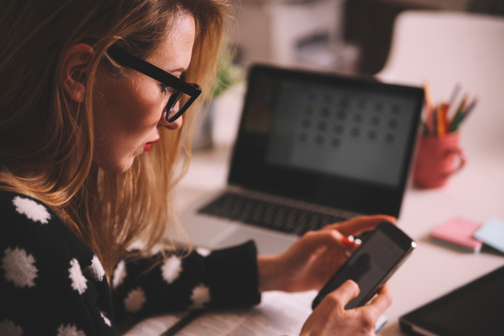 Young blonde woman using Instagram on a smartphone in her creative office space.