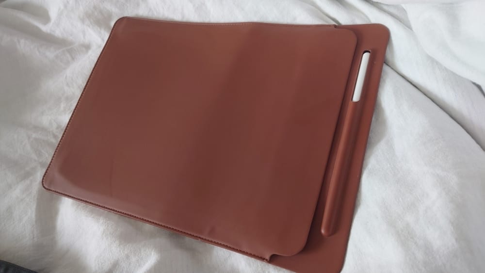 An iPad in a leather case sits on a white bedsheet